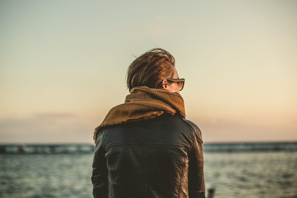 Back of person wearing a leather jacket and scarf while looking at the ocean